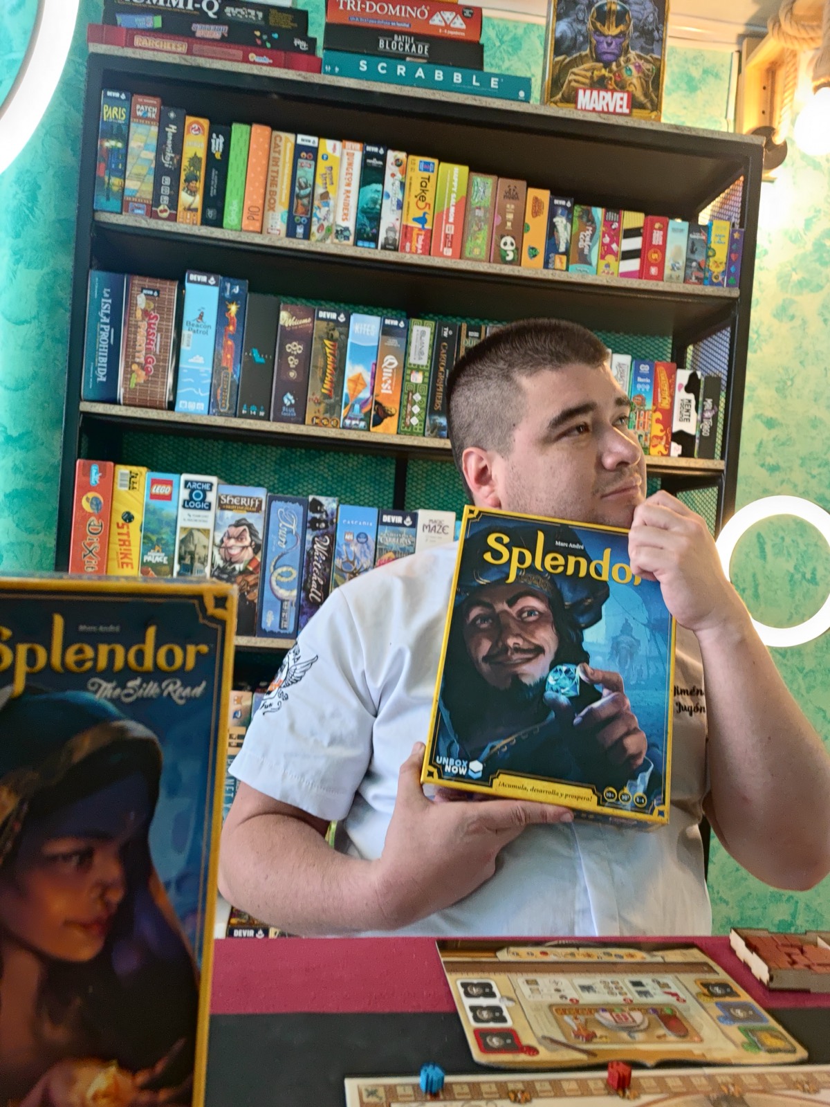 Jugador posando con la caja de Splendor frente a la estantería de juegos